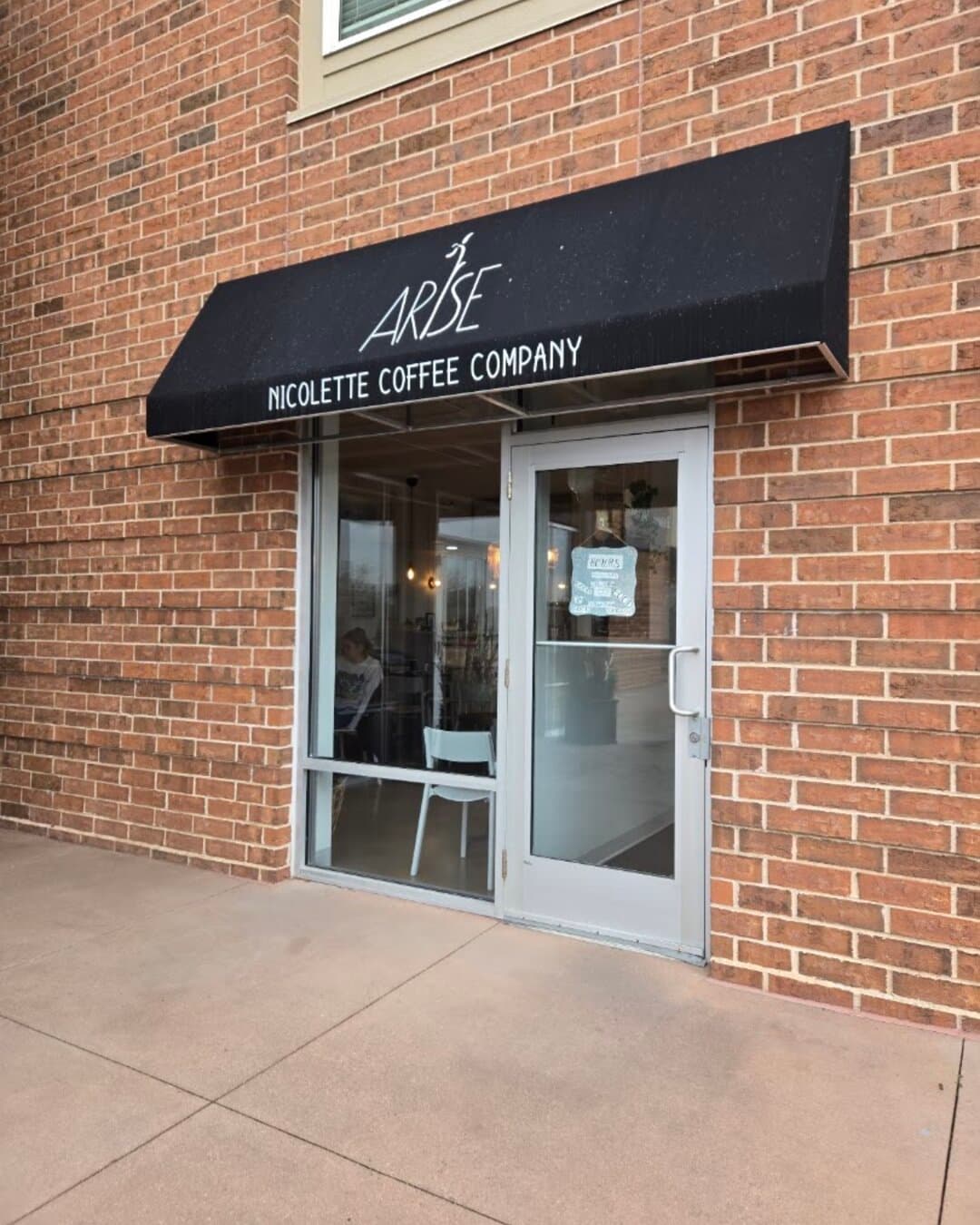The black Arise awning and front door on Nicollet Avenue, red brick around it.
